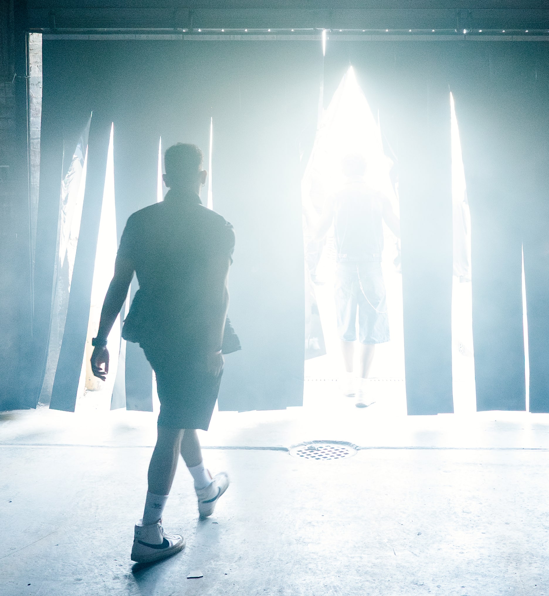 A person walks toward daylight through dark hanging curtains, leaving a smoky indoor party into bright sunlight.