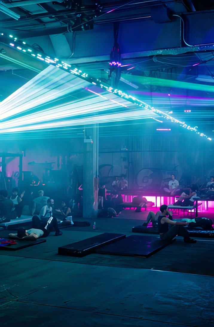 A wide view of the dance space filled with people reclining and chatting under vibrant aqua and magenta lasers.